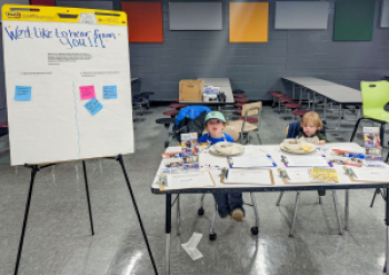 Two young children eat snacks at Owen Middle School, while sitting at the UWABC Community Questions table.