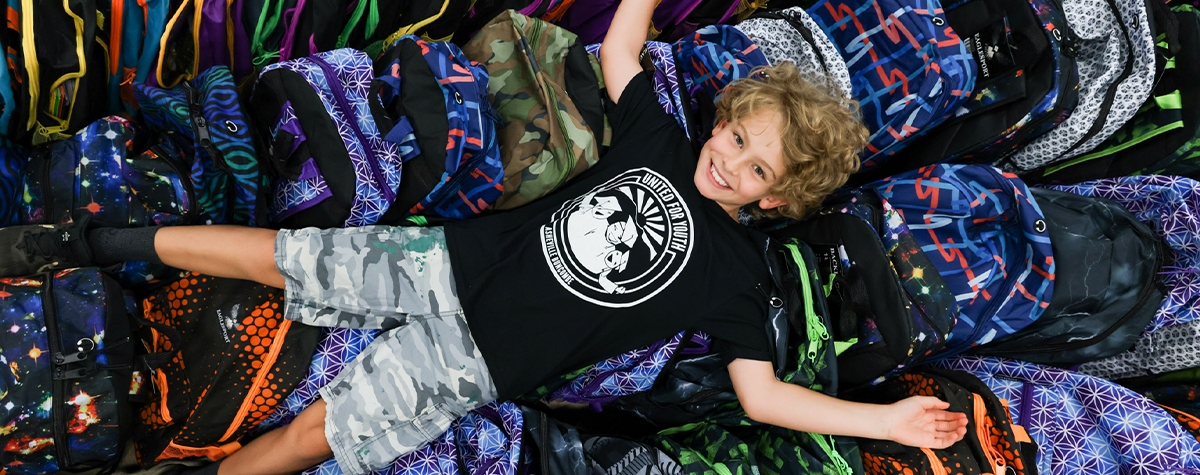 Student lying on fully stocked backpacks.